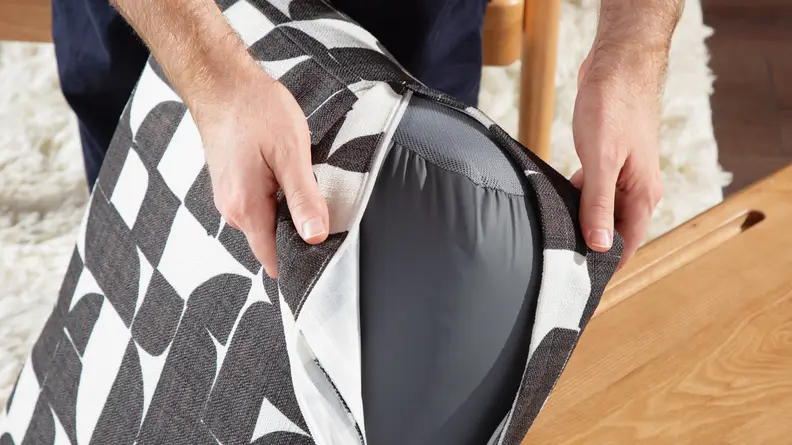 A pair of hands holding a cushion piece and a cover for it.