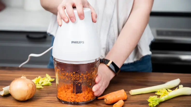 A person is pressing down a mini food processor to get it to work, which seems to be chopping carrots.