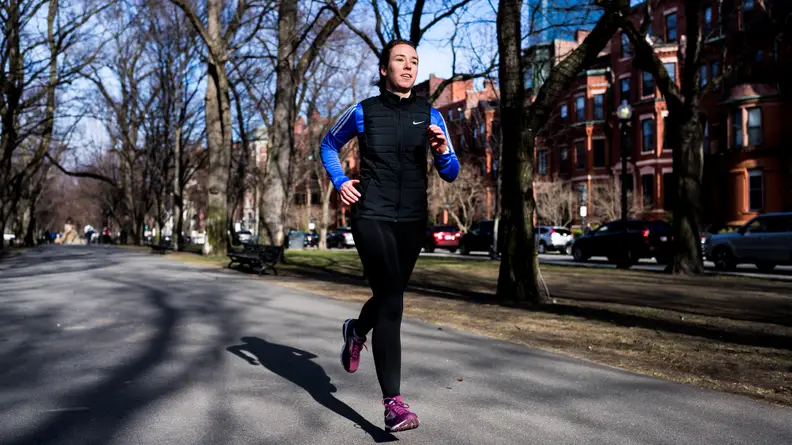 A woman running down the street wearing a Nike vest.