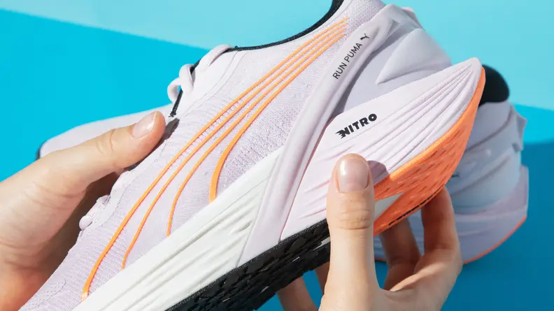 A person grips the underside of a white running shoe.