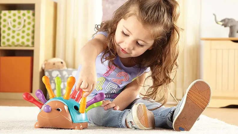 A child plays with a colorful plastic hedgehog on the ground.