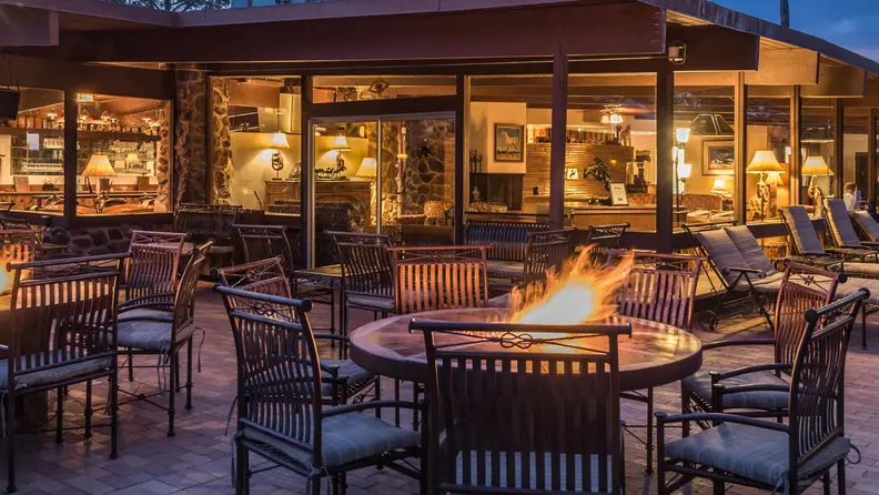 Outdoor lodge patio with fire pits, lounge seating, and warm lighting at dusk.