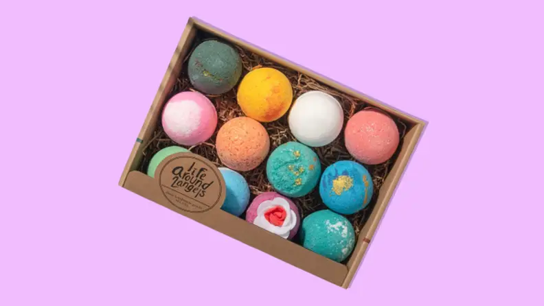 A cardboard box filled with 12 colorful bath bombs in front of purple background.