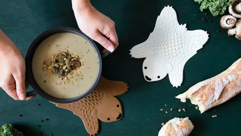 White and brown bear trivets next to loaf of bread with hands holding a pot of soup