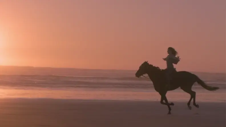 A still from Black Beauty featuring the horse and Jo riding together on the beach.
