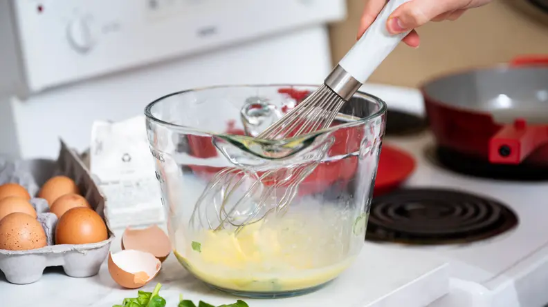 A person whisks together the ingredients for an omelette in a glass bowl.