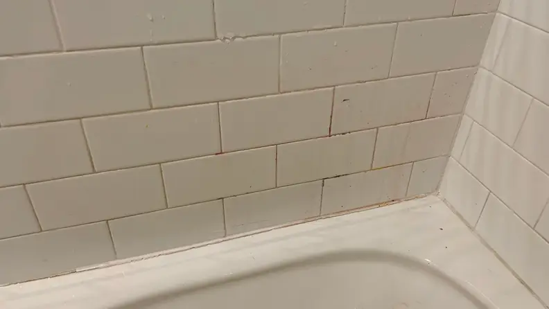 The grout on a bathroom wall is stained with crayon.
