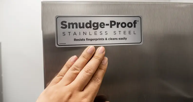 A hand reaches up to the face of the Frigidaire Gallery GRSC2352AF side-by-side refrigerator, unsuccessfully attempting to smudge it.