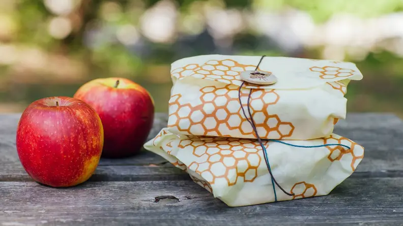 Two apples next to two sandwiches wrapped in bee's wrap