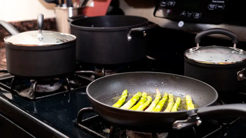 Asparagus cooking in a T-fal frying pan on a gas stove