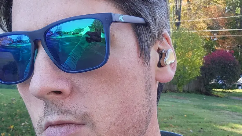 A man wearing sunglasses has an earbud in his ear