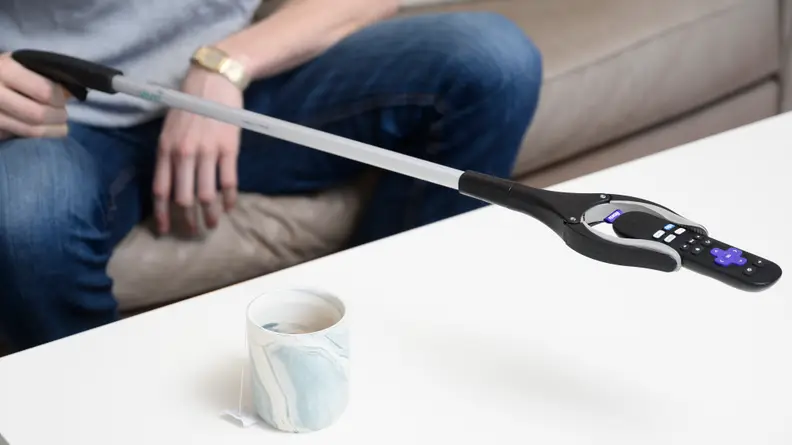 A person uses a reacher grabber to pick up a TV remote