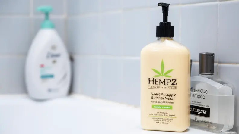 A yellow bottle of Hempz Moisturizing Skin body lotion standing on the side of a tub.
