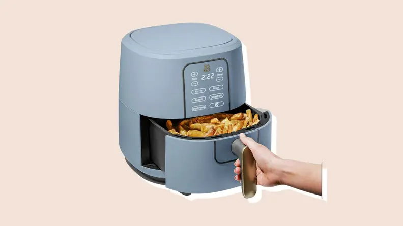 Hand pulling out basket on the light blue air fryer from the Beautiful by Drew Barrymore Kitchen Appliances line.