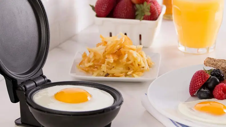 A single egg cooks on the Dash Mini Griddle, surrounded by other cooked eggs plated and ready to eat.