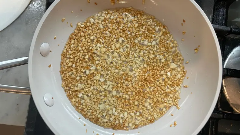 Minced garlic being fried in a skillet.