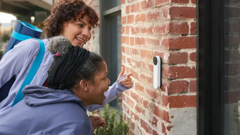 Two smiling people talk into smart doorbell outside of home.