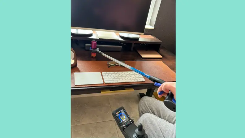 A man in a wheelchair using an RMS reacher grabber to grab a cylinder-shaped object