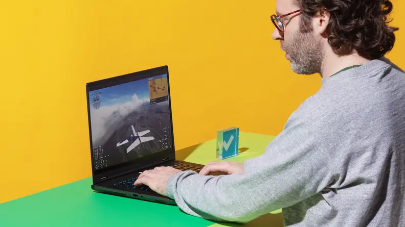 A person sitting at a two-tone green and yellow desk while typing on the Alienware m16 R2 gaming laptop.