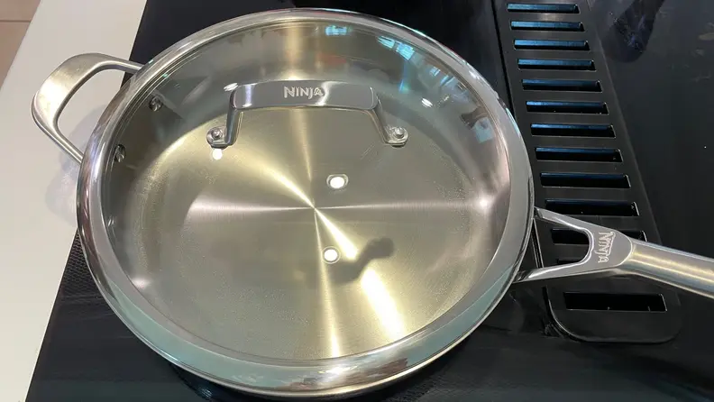 A stainless steel pan and lid on a black stove top.