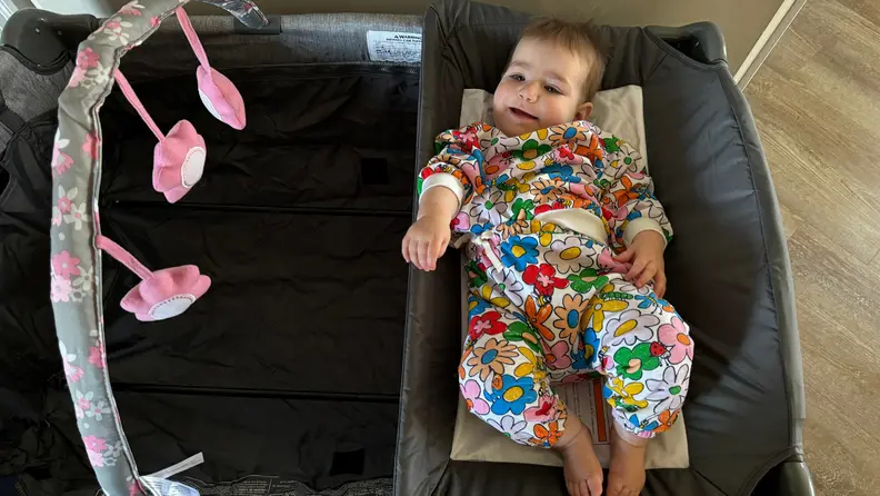 A small toddler lays on top of a changing table inside of the Evenflo pack n' play.