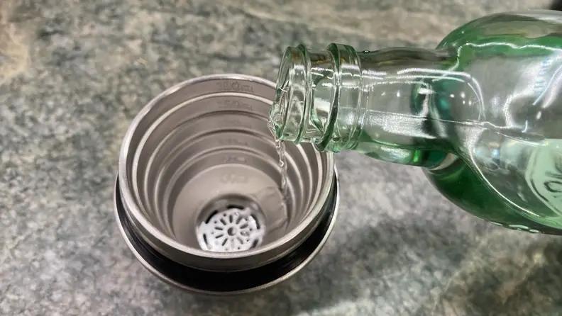 A person pours clear alcohol into a jigger.