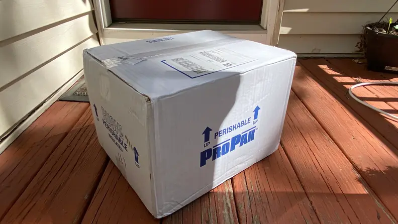 A white cardboard box is placed on a red porch.