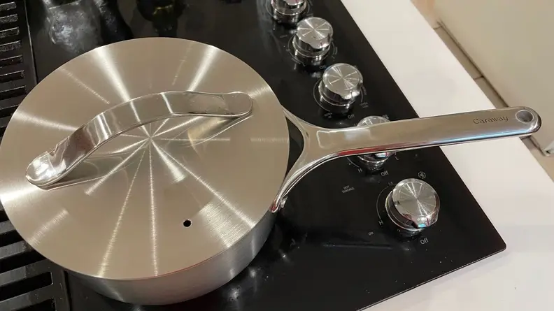 Stainless steel pot with lid on top on top of cooktop.