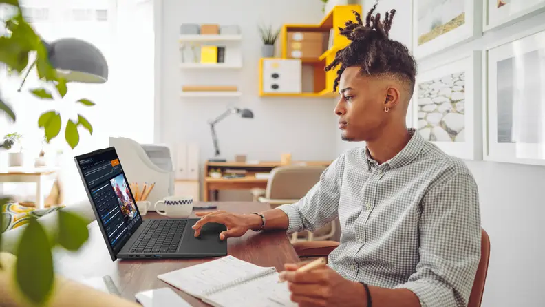 A person seated at their home office desk holds a pencil in their left hand while typing on the keyboard of the Acer Swift Go 16 with their right.