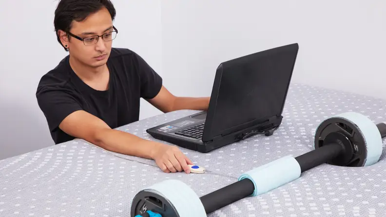 Person conducting a series of tests on the Sealy Posturepedic mattress with a weighted tool and a laptop.