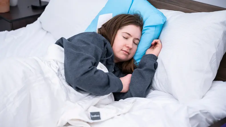 Person laying in bed under covers with pillow under head.