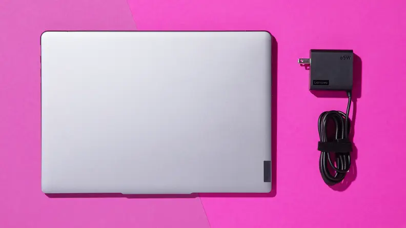 Closed Lenovo Slim 7 laptop next to its power cord on a pink background.