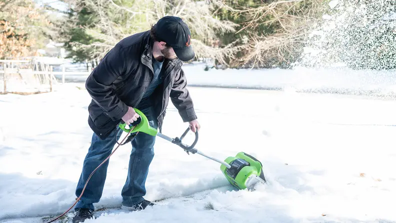 A man clears a path in the snow using the Greenworks Corded Snow Shovel