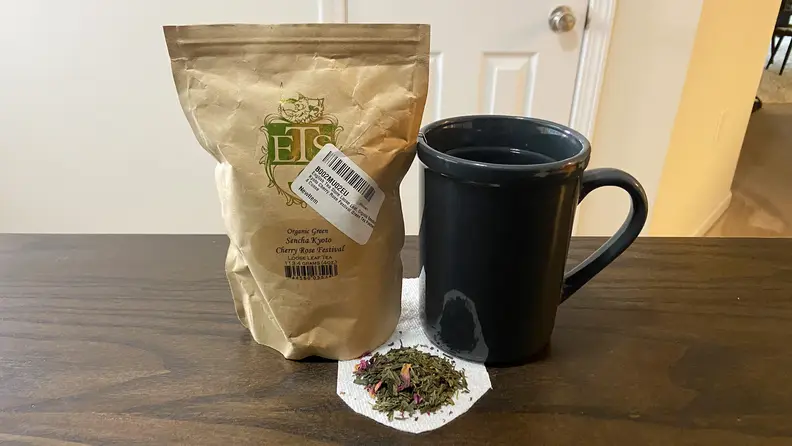 A big of English Tea Store Cherry Blossom Tea sits on a table next to a mug. Tea leaves sit under the mug on a paper towel.