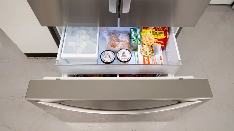 A close-up of the open freezer drawer, stocked full of ice and frozen foods.