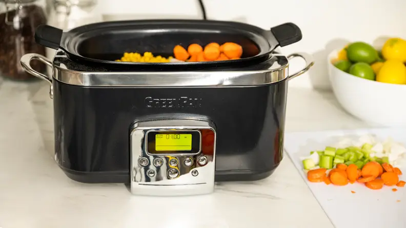 A black GreenPan Slow Cooker is filled with raw vegetables.