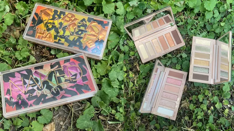 Opened and unopened eye shadow palettes on grass outdoors.