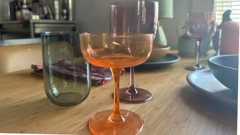 An orange coupe, purple wine glass, and green tumbler on a dining room table.
