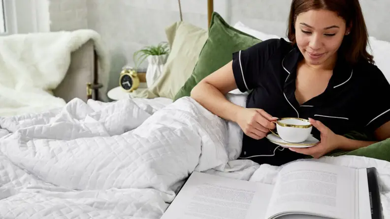 a woman reads in bed under the gravity cooling blanket
