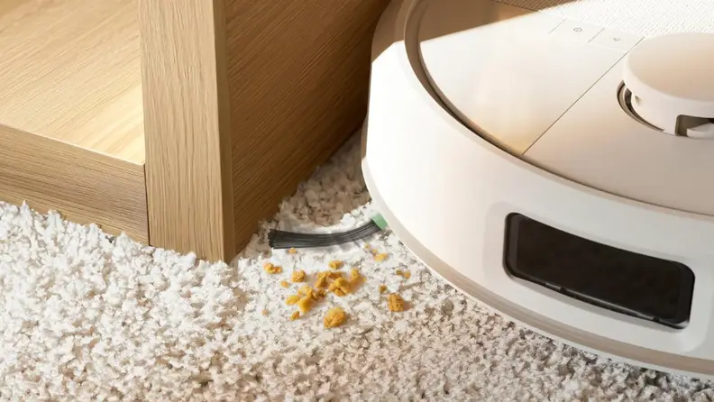 A white robot vacuum sucking up crumbs on a carpet