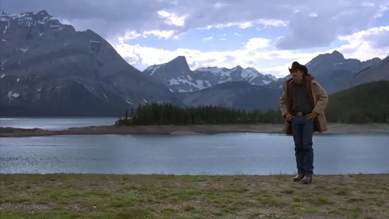 Jack (Jake Gyllenhaal) stands alone beside a river with the mountains in the background.