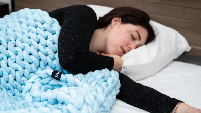 a person sleeps with an arm extended under the Nuzzie weighted blanket