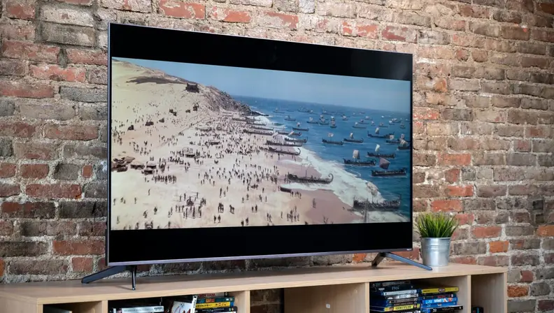 A TCL TV on a media console, showing a scene of a beach war scene.