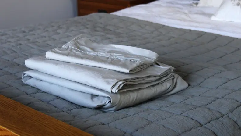 A folded set of percale sheets from Linen Home stacked on the end of a bed.