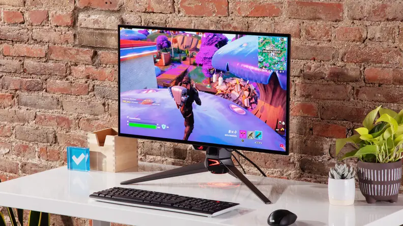 Asus ROG Swift OLED PG27AQDM sitting on top of desk in front of brick wall.