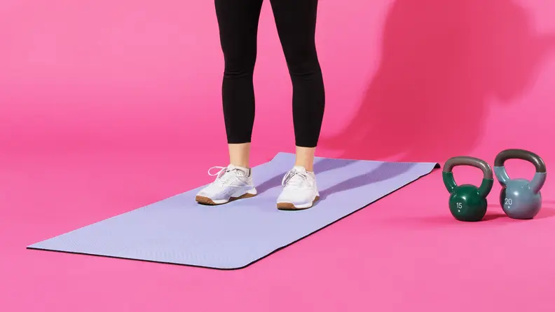 Person standing on top of purple lululemon 5mm workout mat in running sneakers, next to kettlebells.