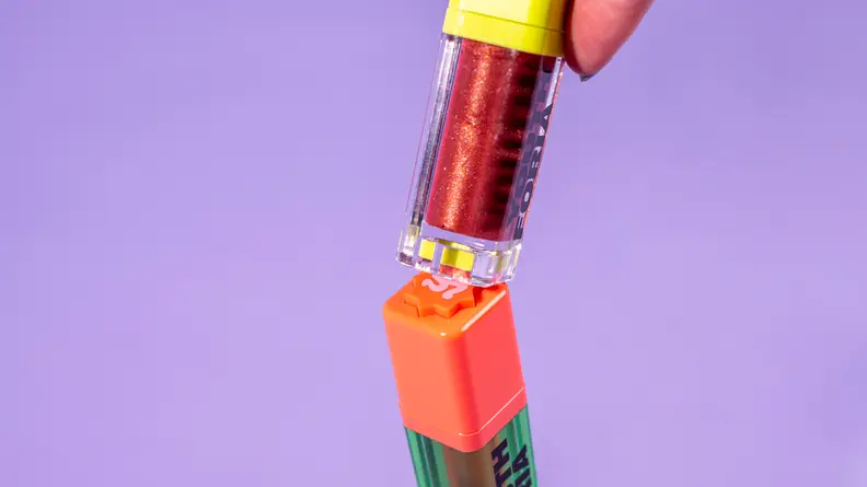 A hand taps The BYO Blush, the bottom tube with orange cap, with the tube of another Youthforia product.