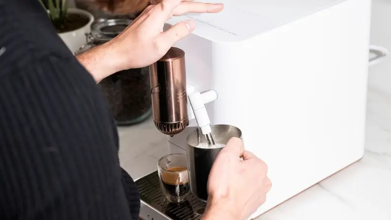Person steaming a jug of milk with the Affetto, with a shot of espresso ready under the dispenser