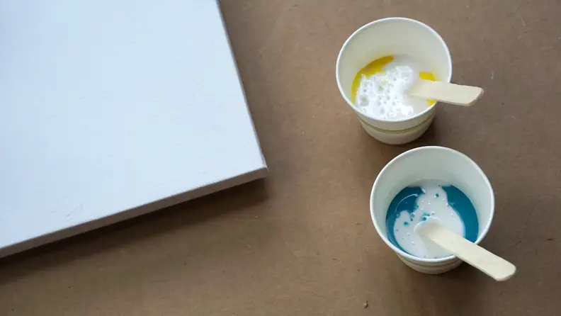 A blank canvas next to paint in cups