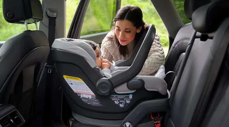 Person crouched near a baby in a car seat in the back of a cat